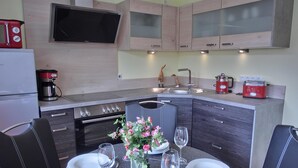 A modern kitchen with a dining area, equipped with a stove, oven, sink, and a flat-screen TV. - 2-zimmer-fewo für 2 Pers. im EG (Graal-Müritz)