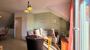 A cozy living room with a sofa, a dining table with chairs, and a kitchen area in the background. - Große, Komfortable 3 Zimmer-maisonette-ferienwohnung für 5 Personen (Graal-Müritz)