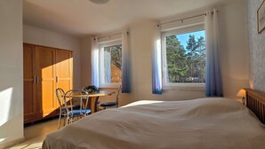 A bedroom with a large bed, a wooden wardrobe, a small table with chairs, and a window with curtains. - Große, Komfortable 3 Zimmer-maisonette-ferienwohnung für 5 Personen (Graal-Müritz)