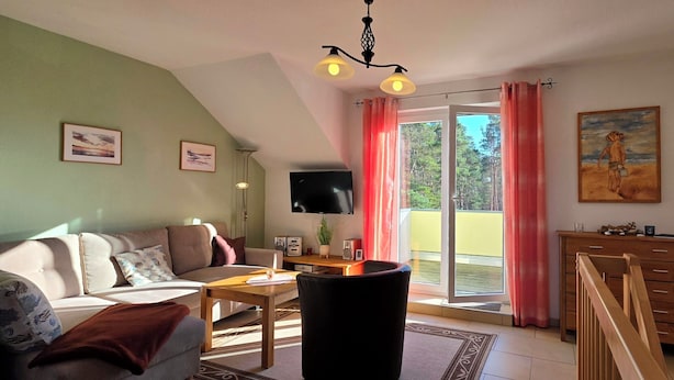A living room with a sofa, a coffee table, a TV, a wooden dresser, and a view of the outdoors through a sliding glass door. - Große, Komfortable 3 Zimmer-maisonette-ferienwohnung für 5 Personen (Graal-Müritz)