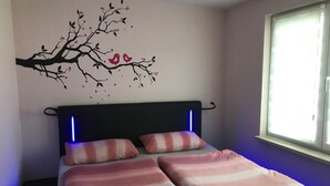 Een slaapkamer met een bed, twee kussens, een wandlamp en een raam.