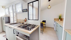 Une cuisine moderne équipée d’une cuisinière à gaz, d’un évier et de placards. Une fenêtre est agrémentée de rideaux décoratifs et un luminaire suspendu éclaire la pièce.