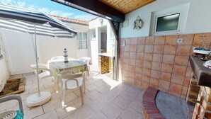 Une terrasse avec une table et des chaises, un petit four en briques et un mur recouvert de carreaux.