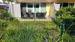 A fenced outdoor area with a table and chairs, a covered seating area, and a building with a yellow facade in the background. - 2-zi.-fewo im EG für 3 Pers. mit Wlan (Graal-Müritz)
