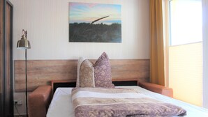 A neatly made bed with patterned bedding, a wooden headboard, and a painting of a landscape on the wall. - 2-zi.-fewo im EG für 3 Pers. mit Wlan (Graal-Müritz)