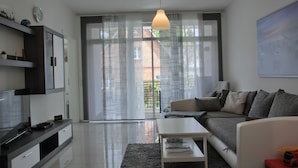 Una sala de estar moderna con un sofá, una mesa de centro, televisor y un balcón con vistas.