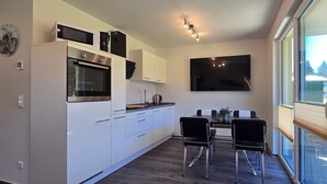 Une cuisine moderne avec des armoires blanches, un four encastré et un coin repas comprenant deux chaises noires et une table.