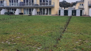 Une rangée de bâtiments modernes à deux étages, dotés de balcons, un jardin verdoyant et des toilettes mobiles.