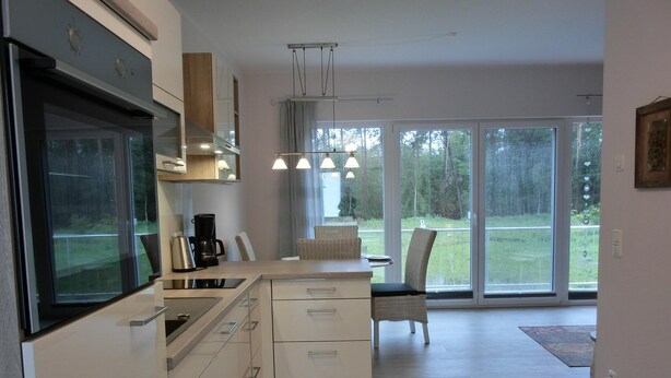 Een moderne keuken met een inbouwoven, een koffiezetapparaat en een eethoek met een stoel en tafel.