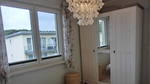 Een slaapkamer met een bed, een kledingkast, een raam met gordijnen en uitzicht op een gebouw.