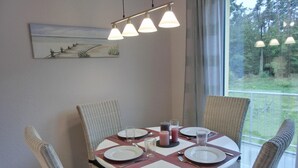 Een eettafel voor vier personen, met rieten stoelen, een schilderij erboven en uitzicht op het landschap.