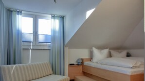 A small, modern bedroom with a bed, a sofa, and a nightstand. - 2-zimmer-fewo für 3 Pers. im Dachgeschoss (Graal-Müritz)