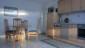 A kitchen with wooden cabinets, a microwave, a dishwasher, and a dining table with chairs. - 2-zimmer-fewo für 3 Pers. im Dachgeschoss (Graal-Müritz)