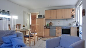 A modern kitchen with wooden cabinets, a dining area with a table and chairs, and a living room with a sofa and armchairs. - 2-zimmer-fewo für 3 Pers. im Dachgeschoss (Graal-Müritz)