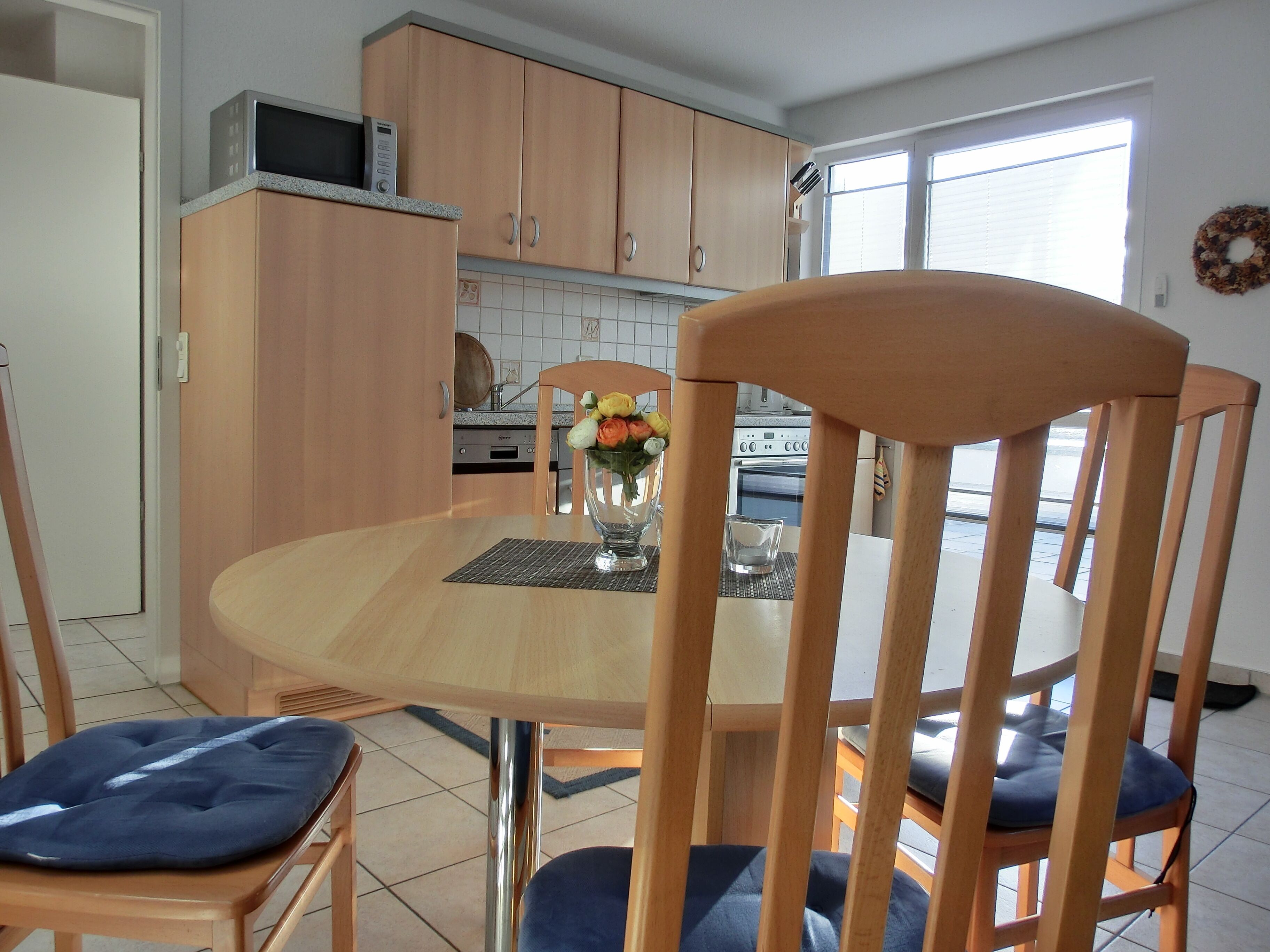 A dining area with a wooden table, chairs, and a vase with flowers.