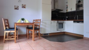 A compact kitchen with white cabinets, a built-in oven, and a microwave. There is a dining table with chairs and a small plant on it. - 2-zi-fewo für 3 Pers. Wlan, Strandnah (Graal-Müritz)