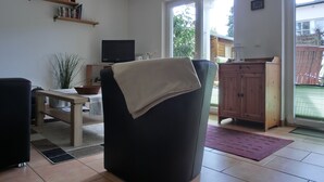 A living room with a black armchair, a television, a bookshelf, and a view of the outside. - 2-zi-fewo für 3 Pers. Wlan, Strandnah (Graal-Müritz)