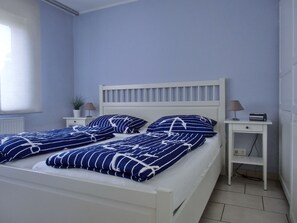 A neatly made bed with blue and white striped bedding, a white headboard, and a bedside table with a lamp and a radio. - 2-zi-fewo für 3 Pers. Wlan, Strandnah (Graal-Müritz)
