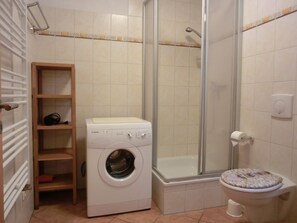 Ein kleines Badezimmer mit Waschmaschine, einer Duschkabine und einem WC.