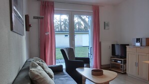 A living room with a sofa, a chair, a small table, a television, and a cabinet. - Modern 2-room vacation apartment for 3 people with bicycles and WLAN (Graal-Müritz)