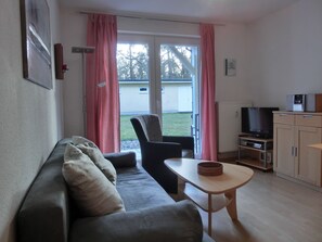 Uma sala de estar com sofá, poltrona, mesa pequena, televisão e um armário.