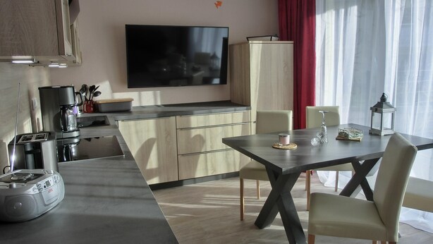 Una cocina moderna con televisión de pantalla plana, cafetera y zona de comedor con mesa y sillas.