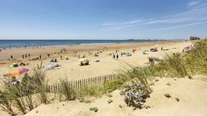 A sandy beach with people, umbrellas, and a wooden fence. - Le Concorde, appartement face mer (Saint-Gilles-Croix-de-Vie)
