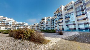 A modern multi-story residential building with balconies, a gravel ground, and some vegetation. - Le Concorde, appartement face mer (Saint-Gilles-Croix-de-Vie)