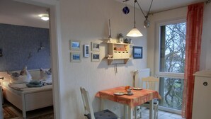 Un coin repas avec une table dressée pour deux personnes, un canapé agrémenté de coussins décoratifs, un radiateur et des tableaux encadrés accrochés au mur.