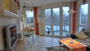 Un salon confortable avec un canapé, une table basse et un coin repas comprenant une table et des chaises. Une grande fenêtre offre une vue sur l’extérieur.