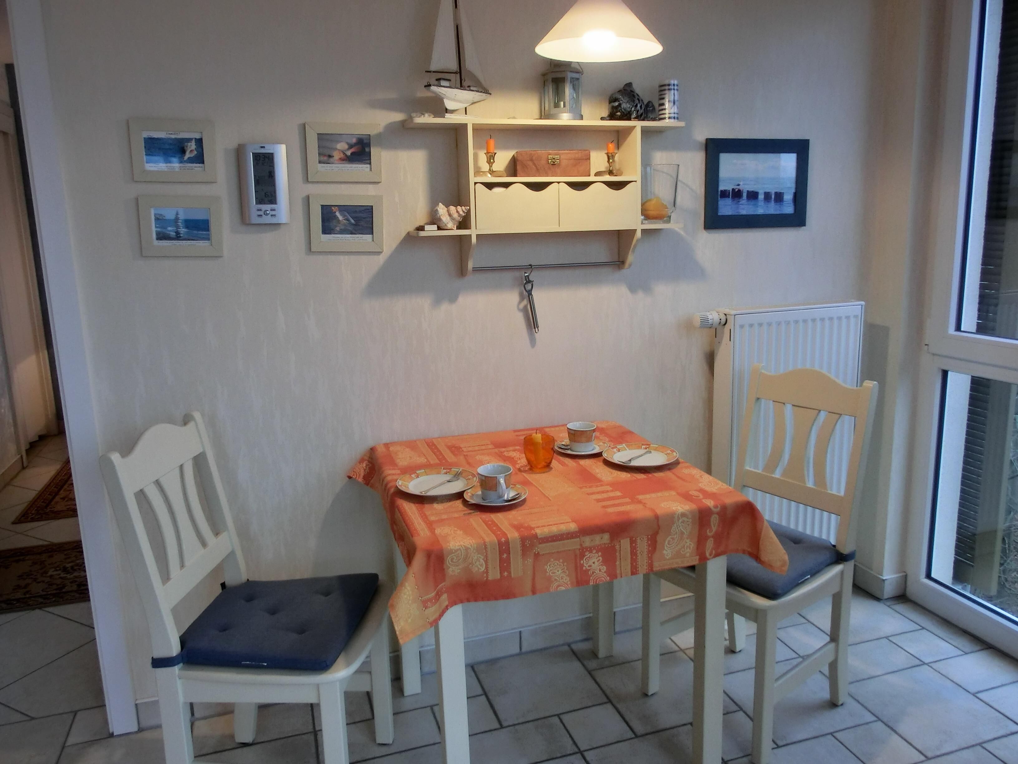 Ein Essbereich mit einem Tisch für zwei Personen, Stühlen, einem Regal mit Dekoration und gerahmten Bildern an der Wand.