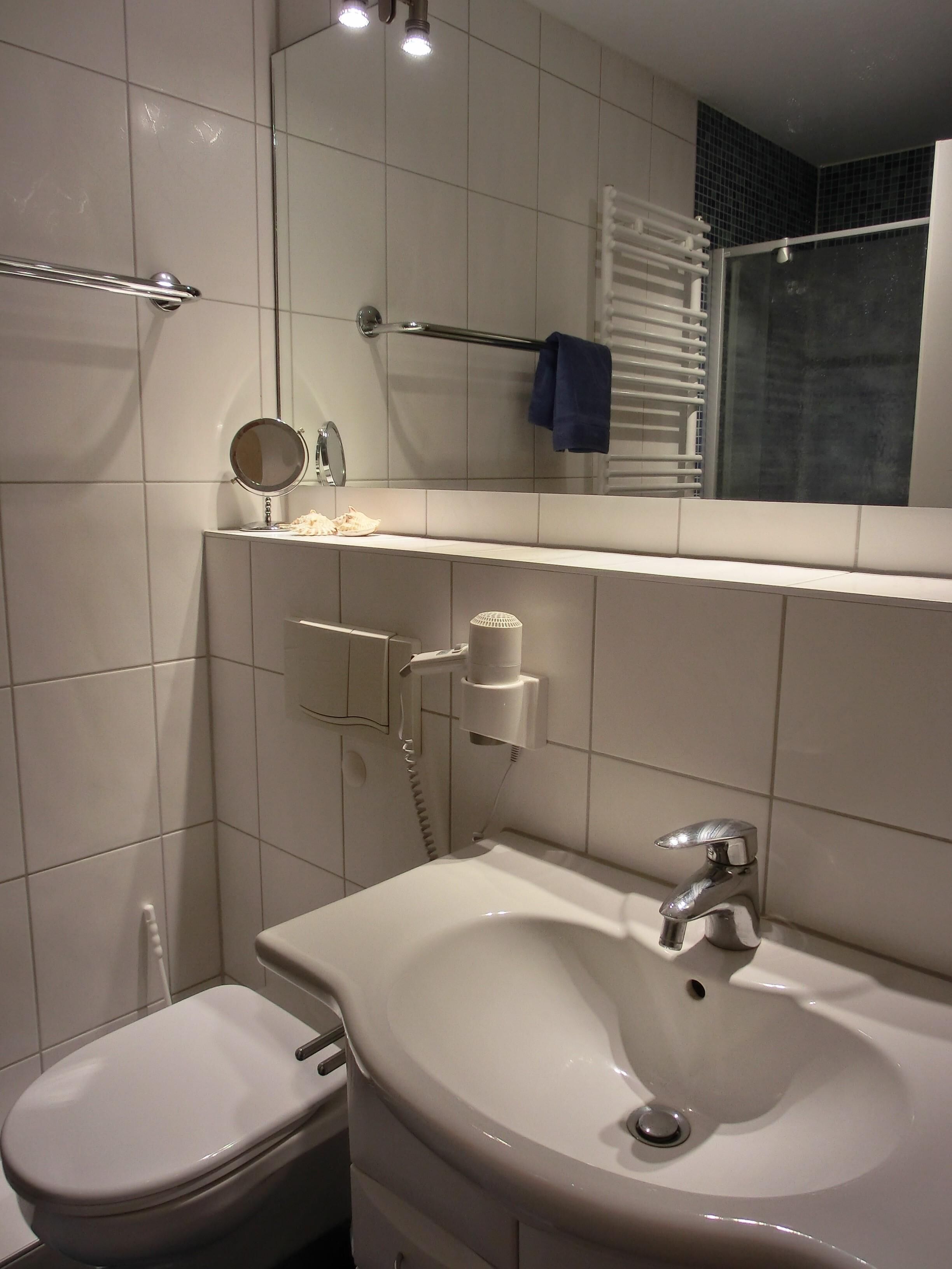A modern bathroom with a white sink, a toilet, a mirror, and a towel rack.