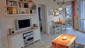 Un salon comprenant un téléviseur, une bibliothèque, un coin repas et de grandes fenêtres.