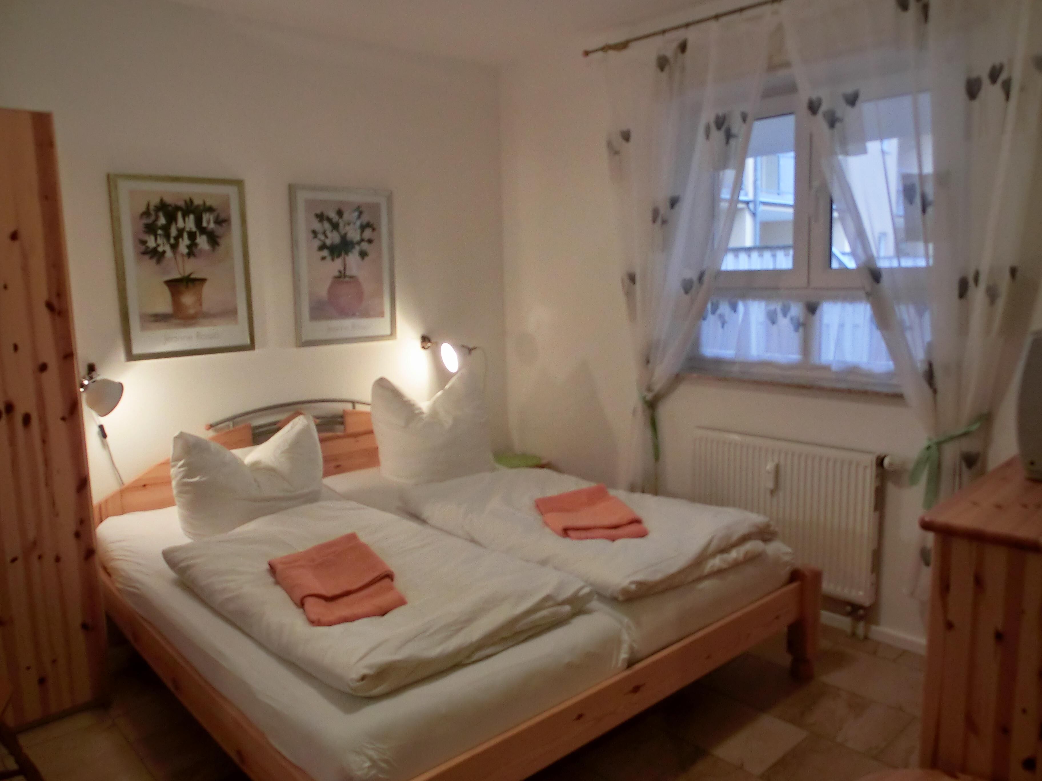 Ein Schlafzimmer mit zwei Betten, weißen Leinen, einem Holz-Kopfteil, einem Fenster mit durchsichtigen Vorhängen und zwei Wandleuchten.
