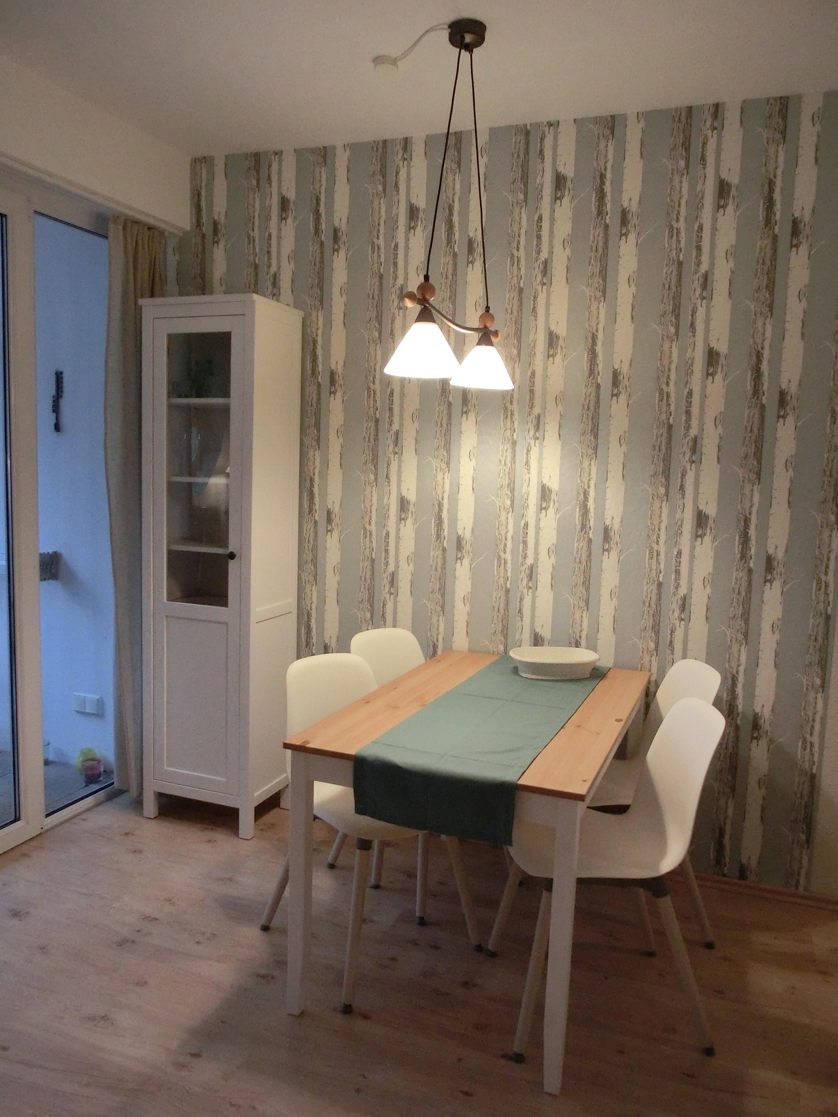 Ein Essbereich mit Holztisch, weißen Stühlen, einem Schrank und wandfarbiger Tapete.