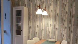Un coin repas avec une table en bois, des chaises blanches, un buffet et un papier peint à motifs.