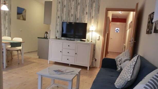 Un salon comprenant un canapé, une table basse, un téléviseur posé sur un meuble et un coin repas avec des chaises.