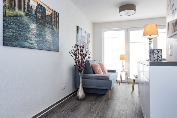 A modern living room with a grey sofa, a vase with dried flowers, and a painting of a cityscape.