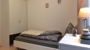Um quarto com uma cama, uma mesa de cabeceira com luminária, um guarda-roupa e duas pequenas quadros na parede.