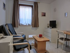 Ein Krankenzimmer mit einem Bett, einem Schreibtisch, einem Sessel, einem Fernseher und einem Fenster mit Vorhängen.