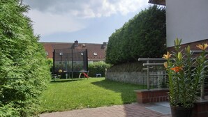 Um quintal com um trampolim, um espaço de recreação infantil e um vaso de planta.