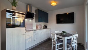 Ett modernt kök med en inbyggd ugn, en platt-TV och en matplats med vita stolar och ett bord.