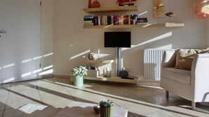 Ein Wohnzimmer mit einer Couch, einem Couchtisch, einem Fernseher, einem Bücherregal und einer Heizung.