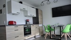 Ett modernt kök med inbyggda vitvaror, en matplats med gröna stolar och en platt-TV som är monterad på väggen.