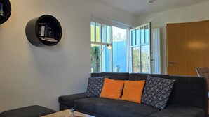 A living room with a dark grey sofa, two orange cushions, a small side table, and two black bookshelves against the wall.
