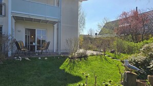 A two-story house with a patio area featuring a table and chairs, surrounded by a well-maintained lawn and garden.