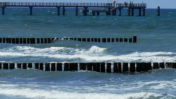A pier extending into the ocean with waves crashing against wooden barriers.