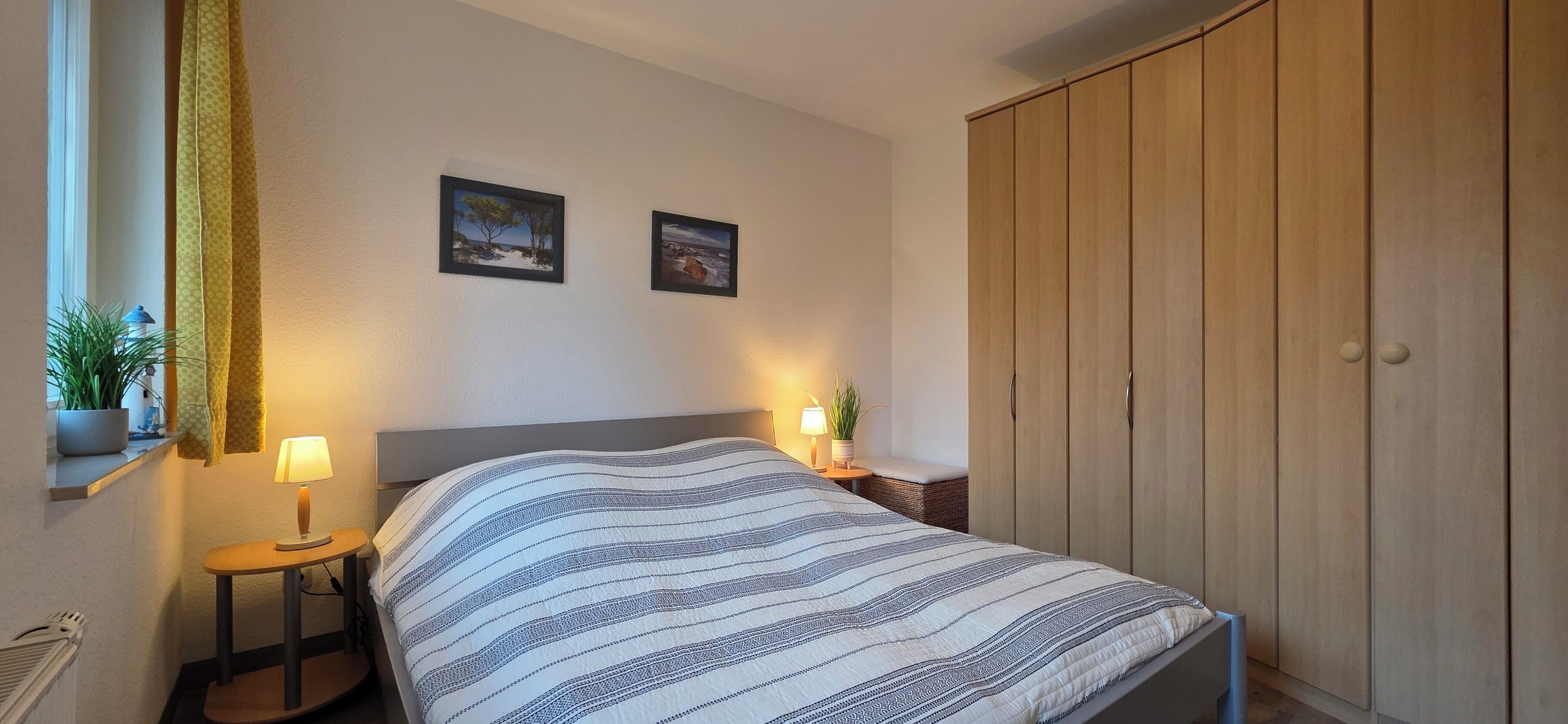 A bedroom with a bed, bedside lamps, a wardrobe, and two framed pictures on the wall.