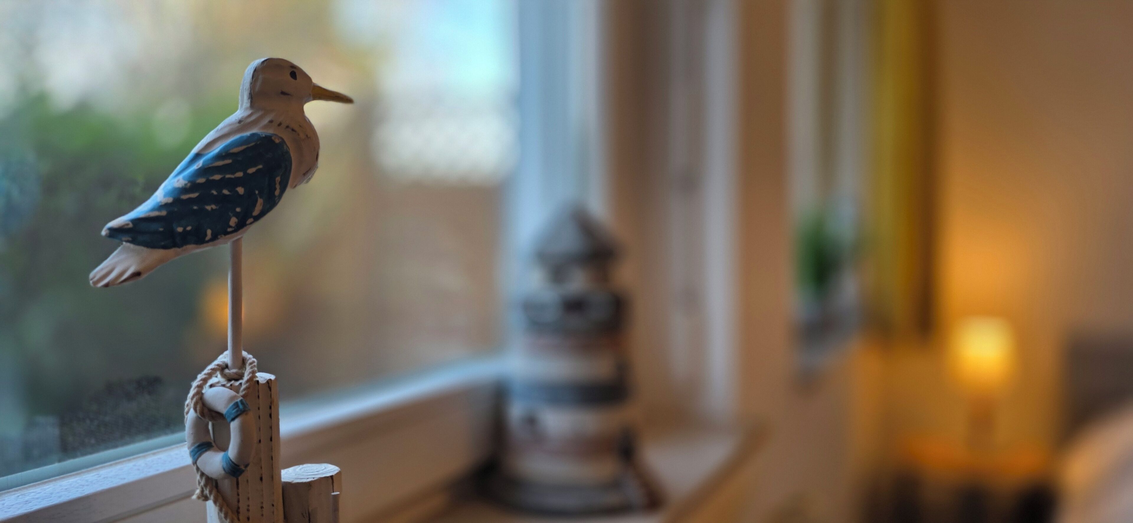 Een vogeltje zit op een houten paal bij een raam.