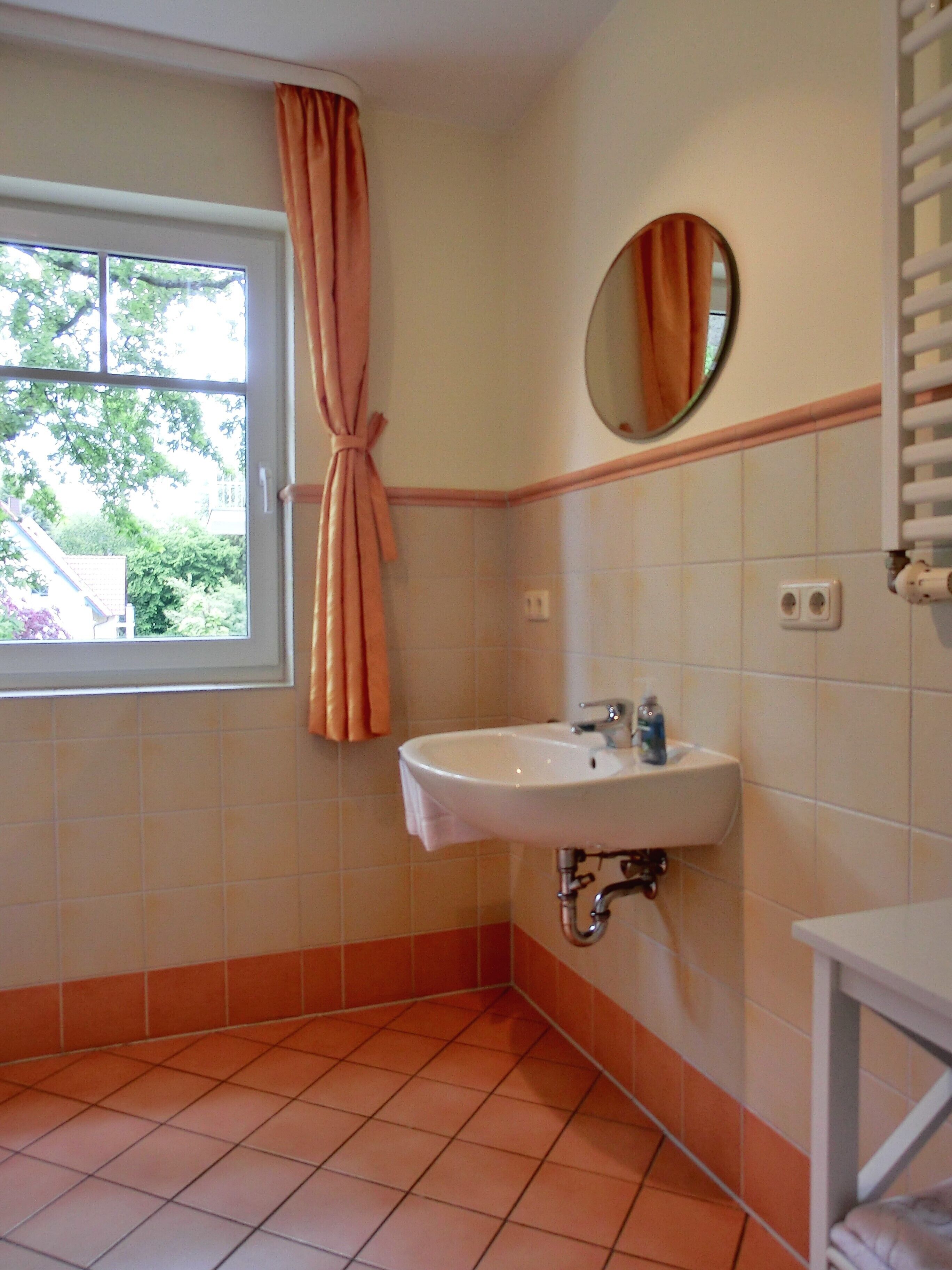 A bathroom with a window, a sink, a mirror, and orange-tiled walls.